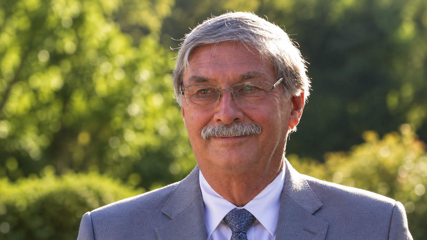 Thomas M. Wells outdoors, with silver hair, glasses, and a warm smile